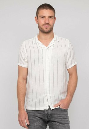 Chemise à manches courtes avec col en tissu blanc à rayures verticales noires. Elle possède une fermeture à boutons et un tissage texturé.