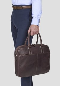Brun læderlaptopbag med dobbelthåndtag, rektangulær form og udvendig lomme. Glat tekstur og diskrete syninger.