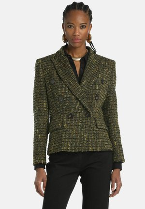 Blazer de doble botonadura en tweed multicolor, con solapas prominentes, dos bolsillos frontales y botones negros. Llevado sobre una camisa negra.