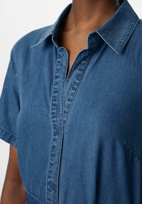 Koszula dżinsowa z klasycznym kołnierzykiem, krótkimi rękawami, zapięciem na guziki oraz miękkim, teksturowanym materiałem w średnim odcieniu niebieskiego.