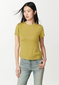 T-shirt a maniche corte, a coste, di colore giallo senape, collo rotondo, texture morbida, abbinato a jeans azzurri chiari.