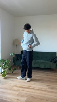 Svjetloplava dukserica s vezicama, prednjim džepovima i rebrastim manžetama, uparen s tamnoplavim širokim hlačama i bijelim tenisicama.