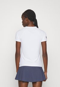 Witte sporttop met korte mouwen en raglanmouwen, gecombineerd met een marineblauwe geplooide rok met een gestructureerd patroon. Glad, lichtgewicht materiaal.