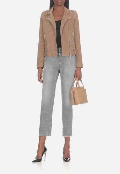 Giubbotto da moto in suede marrone, design aderente, cerniere argentate. Jeans grigi a pois, gamba dritta. Tacchi alti neri in vernice, borsa color sabbia.