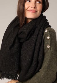 Écharpe tissée noire avec un motif en chevrons, comportant des fils métalliques discrets. Texture douce avec des bords frangés.