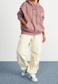 Felpa con cappuccio in rosa tenue, con tasca frontale e cordini. Pantaloni larghi color crema. Sneakers bianche con dettagli blu.