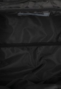 Wnętrze czarnej torby materiałowej o gładkiej fakturze. Posiada zamek błyskawiczny oraz osobną poziomą kieszeń po jednej stronie.