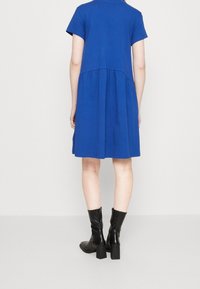 Kortärmad, blå klänning med en samlad midja, tillverkad av mjuk bomull. Buren med svarta ankelboots med en tjock klack och dragkedjestängning.