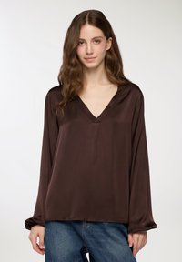 Blusa di raso marrone con scollo a V, maniche lunghe e vestibilità ampia. Presenta una leggera lucentezza e un design pulito e minimale.