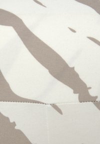 Beige en crème stof met een gladde textuur, voorzien van abstracte, donkerbeige patronen. De naden zijn zichtbaar en benadrukken het ontwerp van de stof.