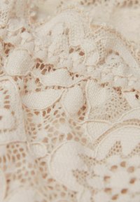 Beige kanten stof met ingewikkelde bloemmotieven, delicate uitsparingen en gestructureerde stiksels, die een gelaagd, lichtgewicht uiterlijk creëren.