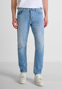 Jeans de mezclilla azul claro con corte recto, cinco bolsillos, pasadores para cinturón y un sutil desvanecido. Combinados con zapatos blancos sobre un fondo neutro.