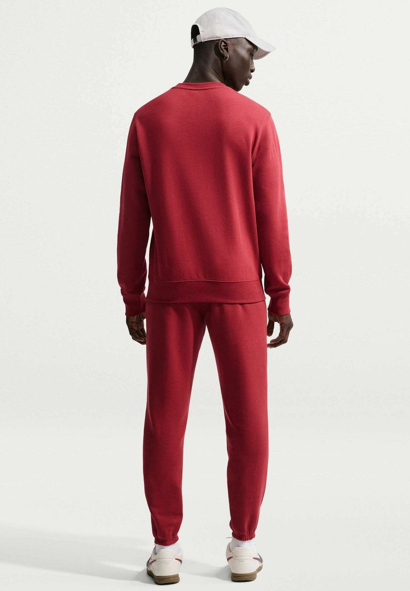 Felpa rossa e pantaloni jogger abbinati realizzati in tessuto morbido, con classico scollo a girocollo, polsini a costine e tasche laterali. Indossati con un cappellino bianco.