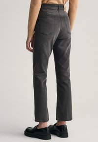 Pantalones de denim gris oscuro con corte recto, cinco bolsillos y una etiqueta de cuero en la cintura. Combinados con zapatos negros.