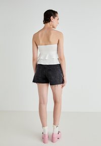 Balta be rankovių peplum bluzonė derinama su juodais nublukintais džinsiniais šortais. Modelis dėvi rožinius platforminius batus ir baltas kojines su nėrinių apdaila.