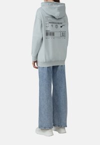 Lichtblauwe oversized hoodie met een capuchon, grafische print op de achterkant en geribbelde manchetten. Gecombineerd met losse, lichtblauwe denim jeans en witte sneakers.