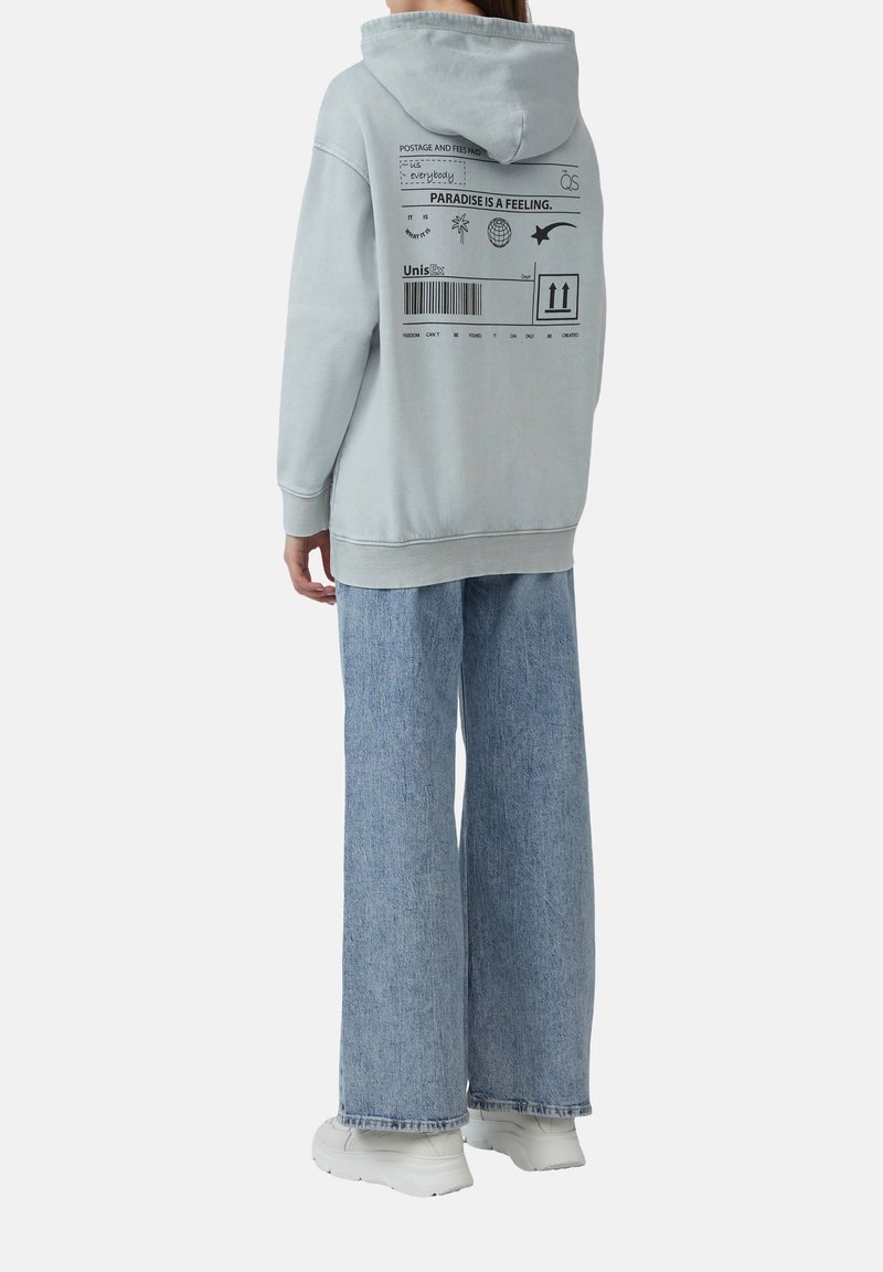 Lichtblauwe oversized hoodie met een capuchon, grafische print op de achterkant en geribbelde manchetten. Gecombineerd met losse, lichtblauwe denim jeans en witte sneakers.