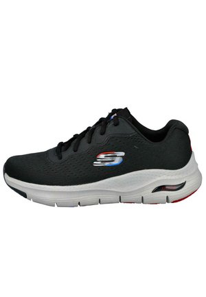 Zapato deportivo negro con parte superior de malla, suela blanca acolchada y un logo "S" multicolor en el costado. Presenta un diseño con cordones y acentos en contraste.