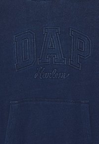Marineblaue Kapuzenjacke mit strukturiertem Stickerei, die "DAP" und "Harlem" zeigt, mit einer Fronttasche und weichem Stoff.