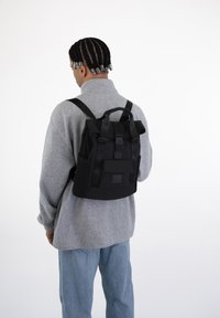 Rucsac negru cu un design structurat, bretele ajustabile, buzunar frontal și buzunare laterale din plasă. Materialul pare durabil și rezistent la apă.