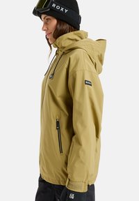 Rumena vodoodporna jakna s kapuco, sprednjim zadrgo in prilagodljivimi vrvicami. Ima črne detajle in logo na rokavu. Črna kapa z logotipom.