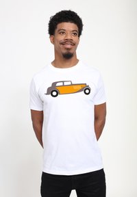Witte katoenen t-shirt met een afbeelding van een vintage auto in bruin en geel, die de zijaanzicht met zwarte wielen illustreert.