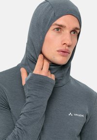 Graues Langarmshirt mit Kapuze, aus strukturiertem Stoff, mit Daumenlöchern und dem "Vaude"-Logo auf der Brust.