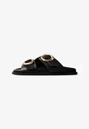 Sandalo slide nero con due ampie fibbie in metallo color oro, suola piatta e finitura testurizzata.