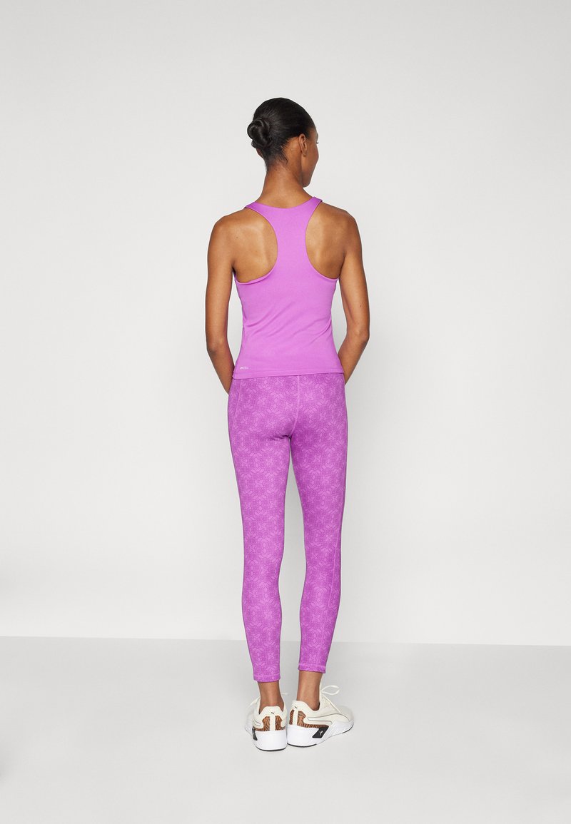 Lila Sporttanktop mit Racerback-Design, kombiniert mit passenden gemusterten Leggings und weißen Sportschuhen. Glatte Textur, figurbetonte Form.