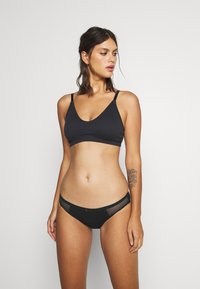 Fekete bordázott bralette állítható pántokkal, hozzá illő fekete bikini hálós részletekkel és díszes masnival az elején.