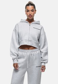 Felpa grigia corta con zip frontale, texture morbida e logo ricamato "GOODFORNOTHING". Abbinata a pantaloni della tuta grigi coordinati.