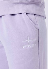Lila sweatpants gemaakt van zachte stof, met een geribbelde tailleband, zijzakken en een witte geborduurde logo op het onderbeen.