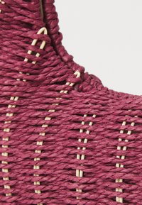 Vevd kurv i dyp burgunder med strukturerte fibre og lyse aksenter. Har en buet design med synlige sømmer og en naturlig finish.