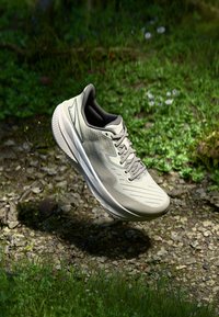 Light gray athletic shoe with a textured mesh upper, padded collar, and laces; the sole features distinct grooves and a contrasting white stripe.