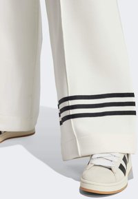 Białe spodnie o szerokich nogawkach z czarnymi bocznymi paskami, połączone z białymi i jasnoszarymi trampkami z czarnymi akcentami i teksturowanym wykończeniem.