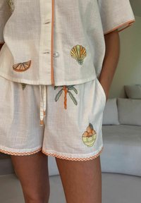 Lina pidžaamakomplekt, millel on lühikesed varrukad, oranž ääris ning värvikas puuviljade ja kestade tikand. Lühikestel pükstel on elastne vöökohal ning taskud.