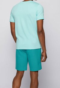 Tyrkysové tričko s krátkým rukávem a odpovídající šortky. Tričko má kulatý výstřih; šortky jsou ke kolenům s ohrnutým lemem. Hladký textilní povrch.