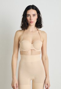 Soutien-gorge beige sans bretelles avec des bonnets moulés et des fines bretelles, associé à des leggings beiges taille haute en tissu lisse et extensible.