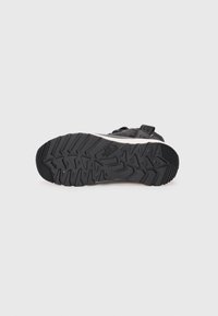 Black hiking shoe sole with deep treads for grip. Features a textured rubber surface and a small logo. Reinforced heel for durability.