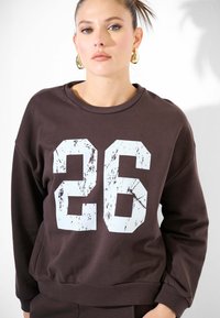 Felpa marrone realizzata in misto cotone, caratterizzata da una grande grafica usurata "26" in azzurro chiaro sul davanti e polsini e orlo a coste.