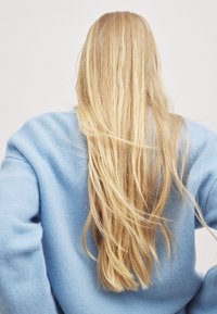 Langes, glattes, blonder Haar, das den Rücken hinunterfällt, getragen mit einem hellblauen, strukturierten Strickpullover. Minimalistischer Hintergrund.