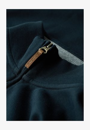 Ciemnogranatowy sweatshirt o fakturowanym wykończeniu, z zamkiem błyskawicznym przy kołnierzu i skórzanym uchwytem wytłoczonym z napisem "Superdry".