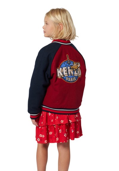 Veste de varsity rouge et bleu marine avec des poignets côtelés, arborant un grand logo imprimé au dos et des rayures contrastées.