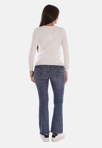 Top bianco a maniche lunghe abbinato a jeans a campana blu scuro. L'outfit è completato da sneakers bianche con dettagli neri e branding.