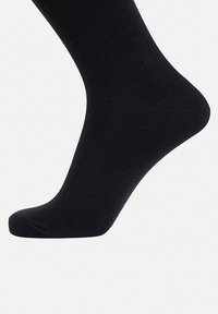 Sort ankelstrømpe lavet af et glat, elastisk materiale med forstærket tå og hæl. Designet er sømløst med et minimalistisk udseende.