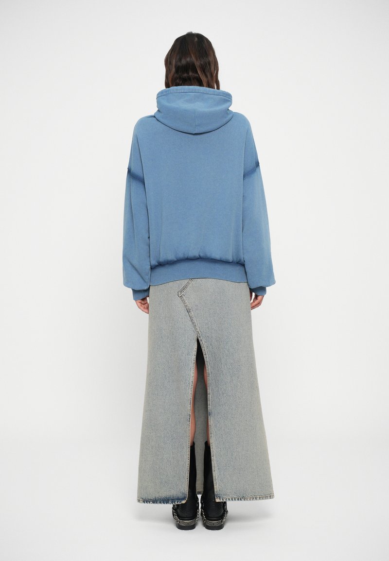 Lyseblå hættetrøje lavet af blødt stof med hætte, parret med en lang, grå denimnederdel med slids bagpå og synlige syldetaljer.