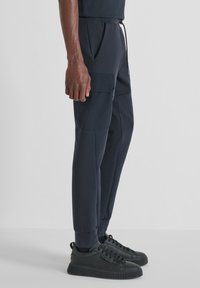 Marineblauwe sweatpants met elastische boorden en zakken. Gemaakt van een gladde, rekbare stof. Gecombineerd met zwarte sneakers met textuurachtige zolen.