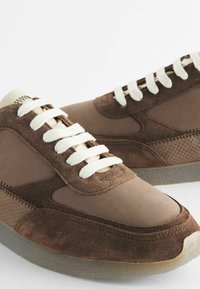 Brune sneakers lavet af læder og ruskind, med hvide snørebånd, perforerede detaljer og en tekstureret sål for godt greb.