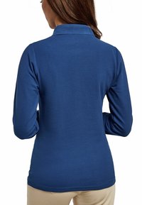 Niebieska polo z długim rękawem, wykonana z gładkiego materiału, z kołnierzykiem i dopasowanym krojem. Tył ma wykończenie o zakrzywionej linii i nie ma widocznych logotypów.