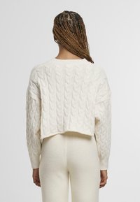 Cream cable-knit cropped sweater with wide sleeves and ribbed cuffs. Soft texture, no visible patterns or hardware details.